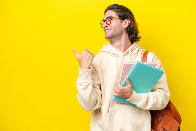 Young student handsome man isolated on yellow background pointing to the side to present a product