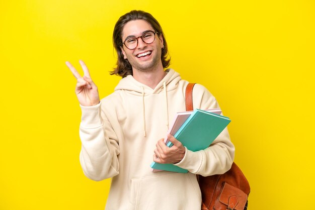 Young student handsome man isolated on yellow background smiling and showing victory sign