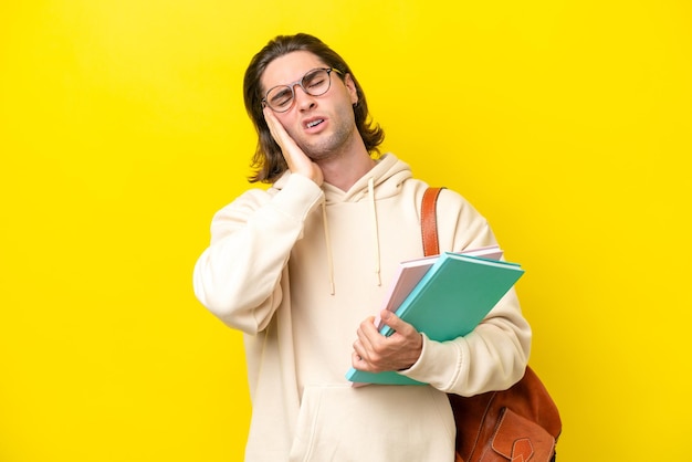頭痛で黄色の背景に分離された若い学生のハンサムな男