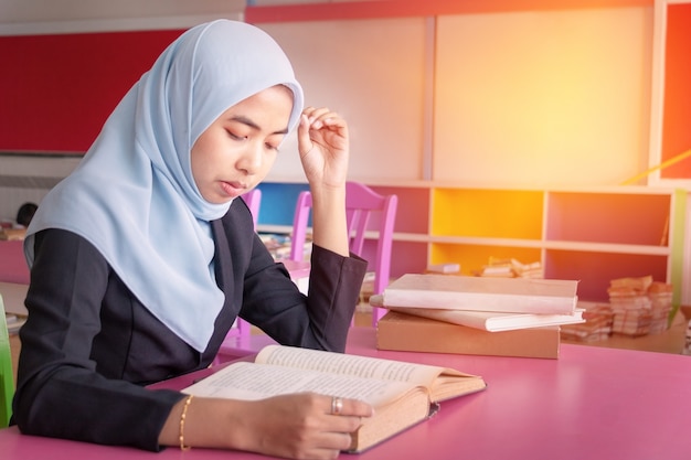 젊은 학생 이슬람 여자. 그녀는 앉아서 책을 읽고 있습니다.