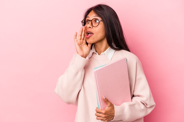 Giovane studentessa latina isolata su sfondo rosa sta dicendo una notizia segreta di frenata calda e sta guardando da parte