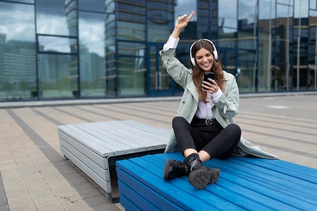 Young student listening to music sitting on a bench in a yoga position dancing against the backdrop