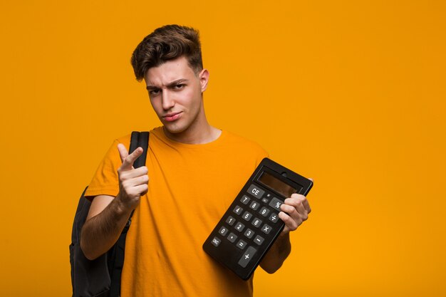 Young student man holding a calculator impressed holding copy space on palm