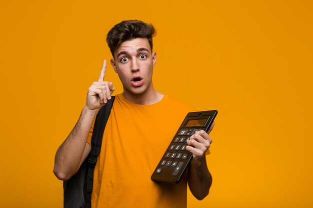 Young student man holding a calculator relaxed thinking about something looking at a copy space.