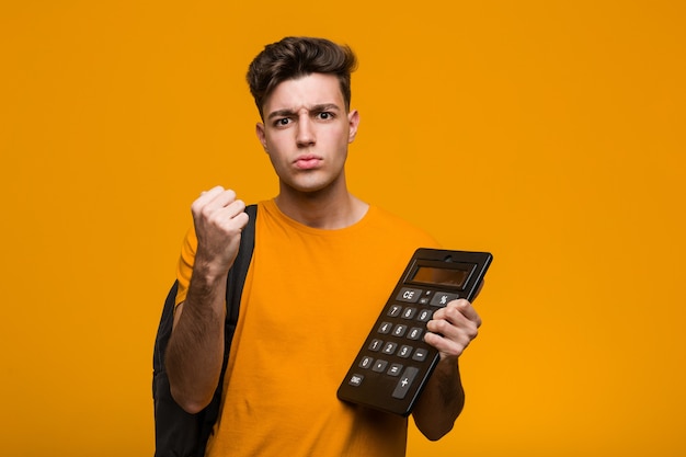 Young student man holding a calculator showing number one with finger.