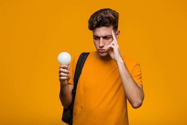 ゴシップを聞いてしようとして電球を保持している若い学生男。