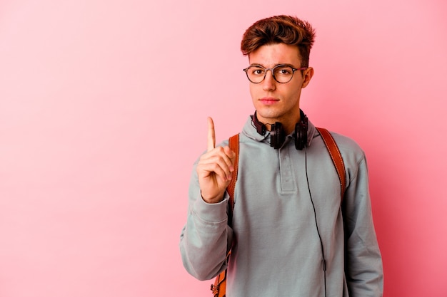 Young student man isolated on pink background showing number one with finger.