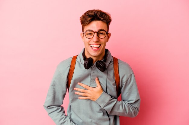 Young student man isolated on pink wall laughs happily and has fun keeping hands on stomach.