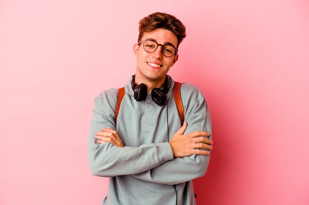 Uomo giovane studente isolato sul muro rosa che si sente fiducioso, incrociando le braccia con determinazione.