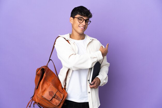 Young student man over isolated purple background pointing back