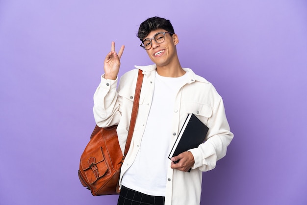 Young student man over isolated purple background smiling and showing victory sign