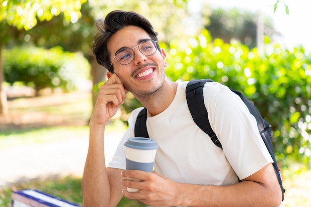 テイクアウトコーヒーを保持している屋外で若い学生の男