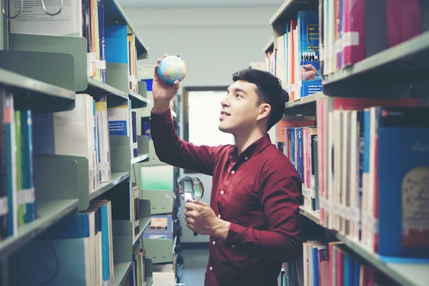 Young student man reading book and holding earth model in hand.