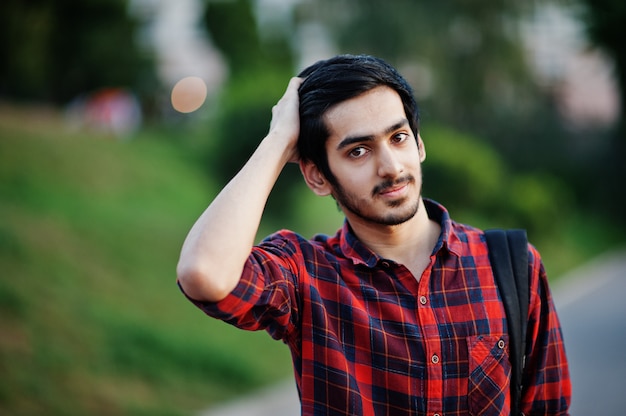 Young student man at red checkered shirt and jeans with backpack posed at street