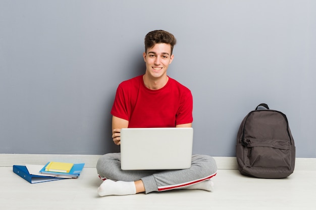 ラップトップを保持している彼の家の床に座っている若い学生男