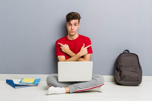 Young student man sitting on his house floor holding a laptop