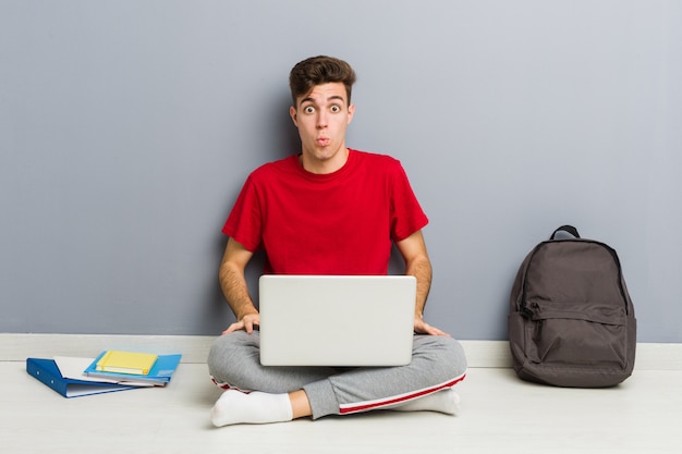 Foto uomo giovane studente seduto sul suo pavimento di casa in possesso di un computer portatile