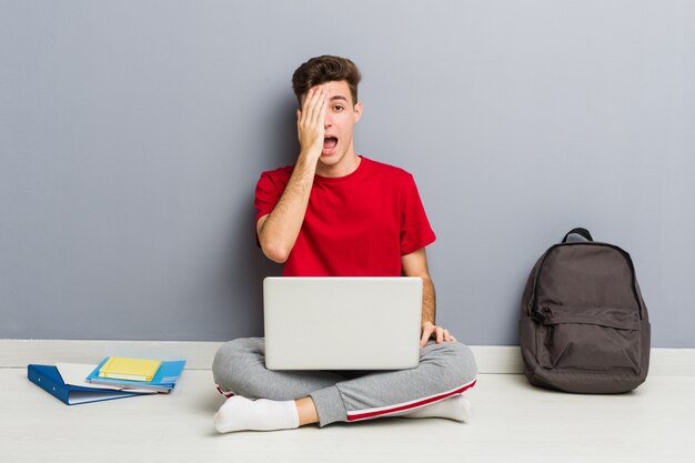 Young student man sitting on his house floor holding a laptop