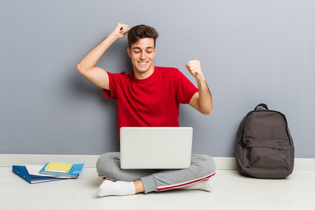 Uomo giovane studente seduto sul suo pavimento di casa in possesso di un computer portatile