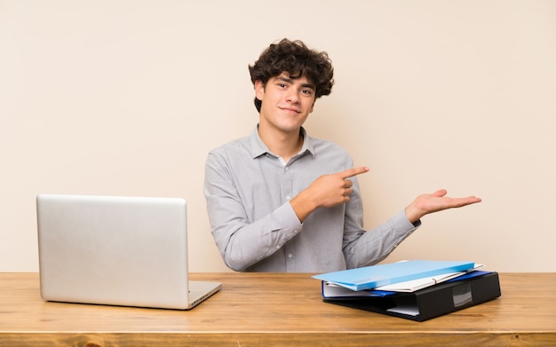 Young student man with a laptop holding copyspace imaginary on the palm to insert an ad