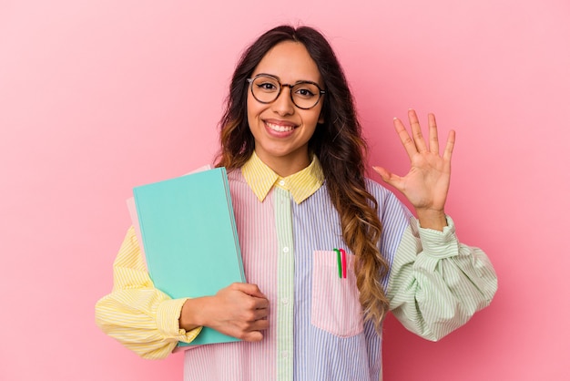 Young student mexican woman isolated on pink background smiling cheerful showing number five with fingers.