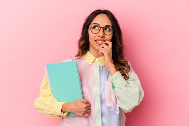 ピンクで孤立した若い学生のメキシコ人女性は、コピースペースを見ている何かについて考えてリラックスしました。