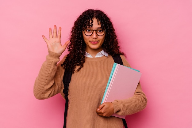 ピンクの笑顔で陽気な若い学生の混血の女性は、指で5番を示しています。