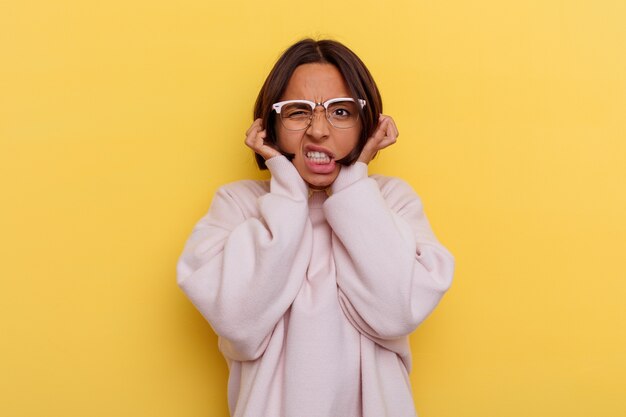 Young student mixed race woman isolated on yellow background covering ears with hands.