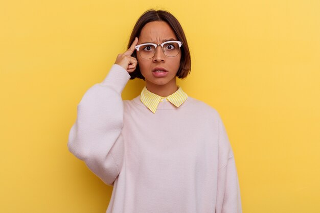 Young student mixed race woman isolated on yellow background pointing temple with finger, thinking, focused on a task