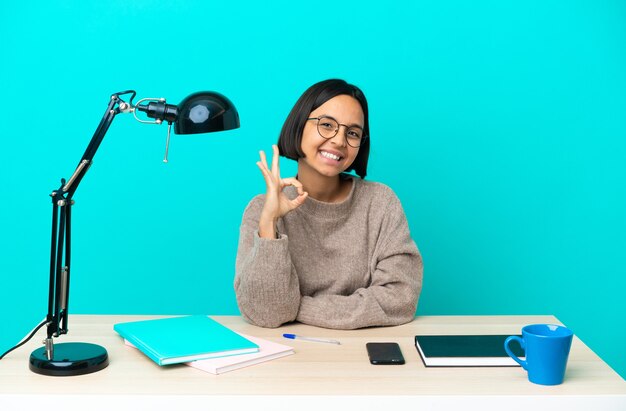 Young student mixed race woman studying on a table showing ok sign with fingers