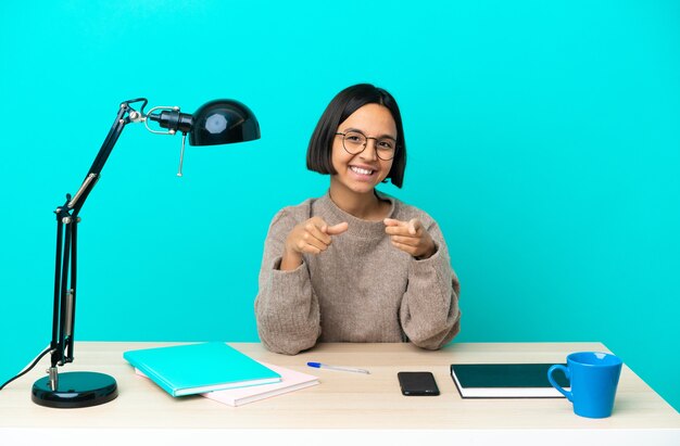 Young student mixed race woman studying on a table surprised and pointing front