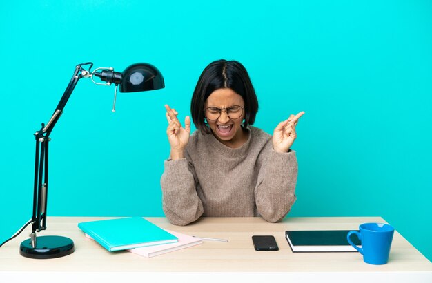 Young student mixed race woman studying on a table with fingers crossing