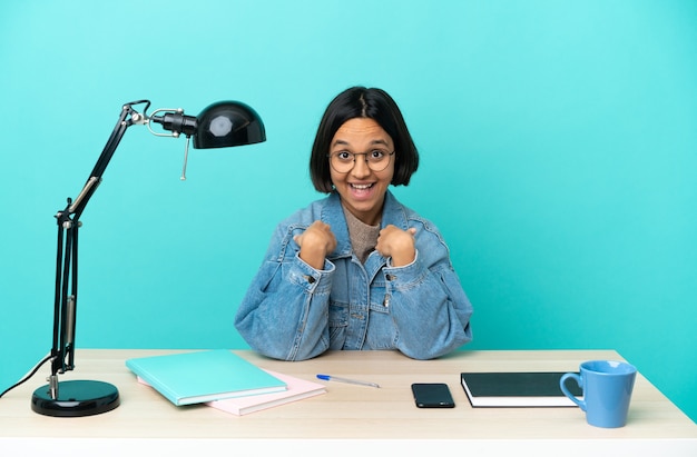 Young student mixed race woman studying on a table with surprise facial expression