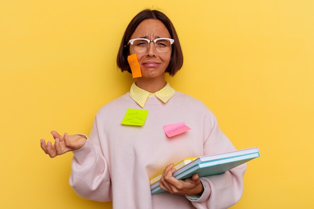 Young student mixed race woman very busy isolated on yellow wall