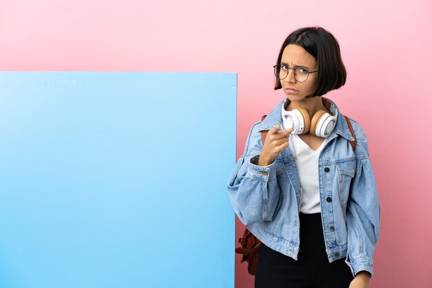 Young student mixed race woman with a big banner over isolated background frustrated and pointing to the front