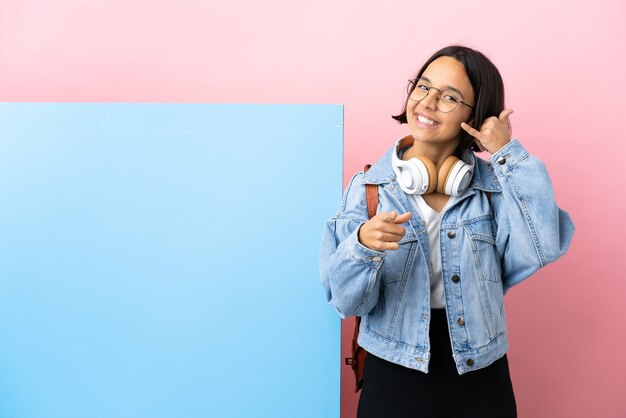 Young student mixed race woman with a big banner over isolated background making phone gesture and pointing front