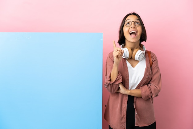 Young student mixed race woman with a big banner over isolated background pointing up and surprised