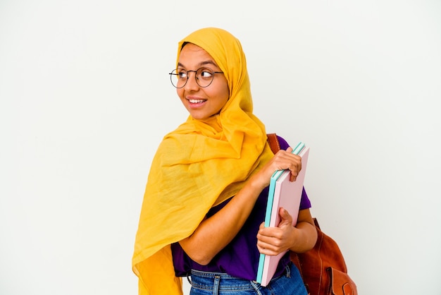 Photo young student muslim woman wearing a hijab isolated on white wall looks aside smiling, cheerful and pleasant.