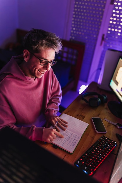 Young student in pink sweatshirt and glasses having fun reading her notebook in the room