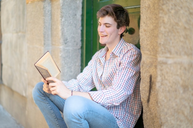 Young student reading a book on the stairs of a building