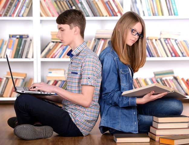 Young student reading a book and using a laptop.