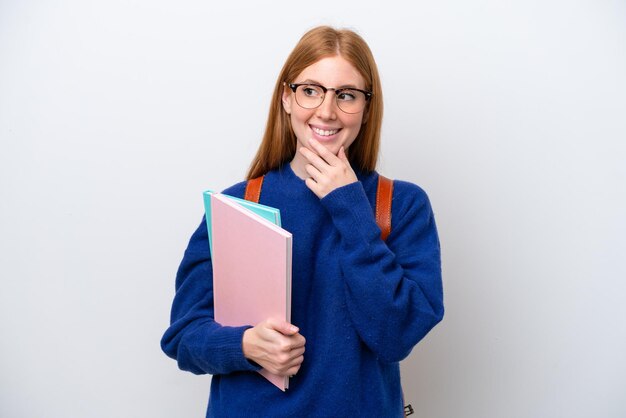 Young student redhead woman isolated on white background
looking up while smiling