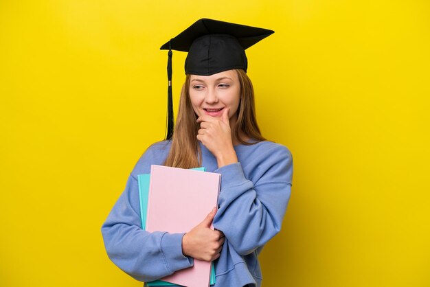 横を見て笑っている黄色の背景に分離された若い学生ロシア人女性