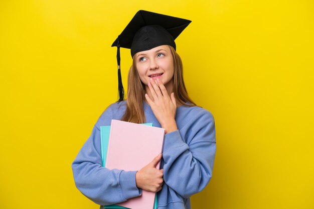 Young student russian woman isolated on yellow background looking up while smiling