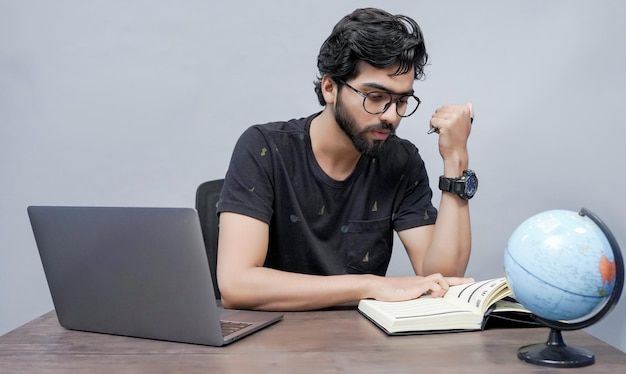 young student sitting on the table using laptop for working on grey wall indian pakistani model