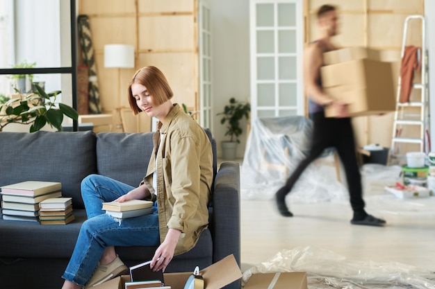 Young student taking book out of box against blurry outline of male loader