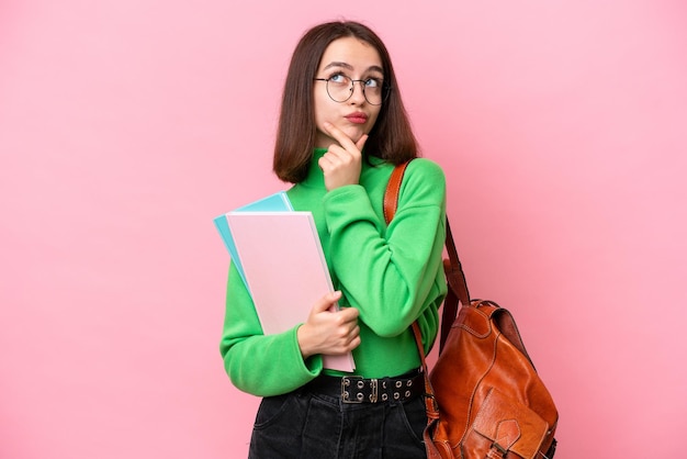ピンクの背景に孤立した若いウクライナの学生が疑問を抱いている