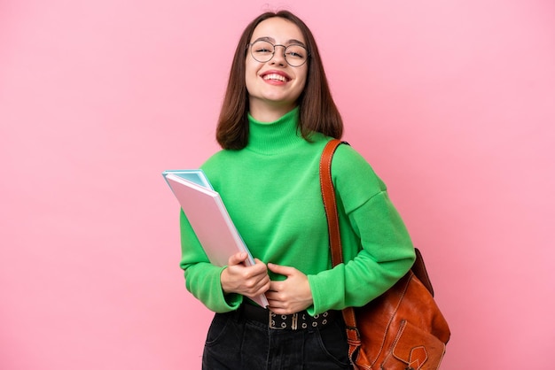 ピンクの背景に孤立した若い学生のウクライナの女性は、たくさんの笑顔を浮かべています