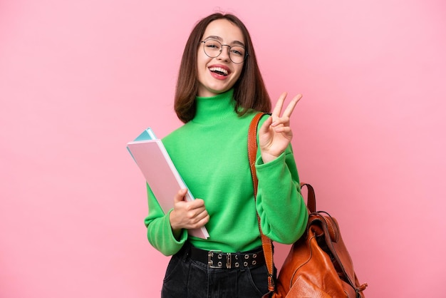 Young student Ukrainian woman isolated on pink background smiling and showing victory sign
