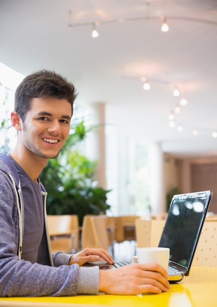 Молодой студент, используя свой ноутбук в кафе